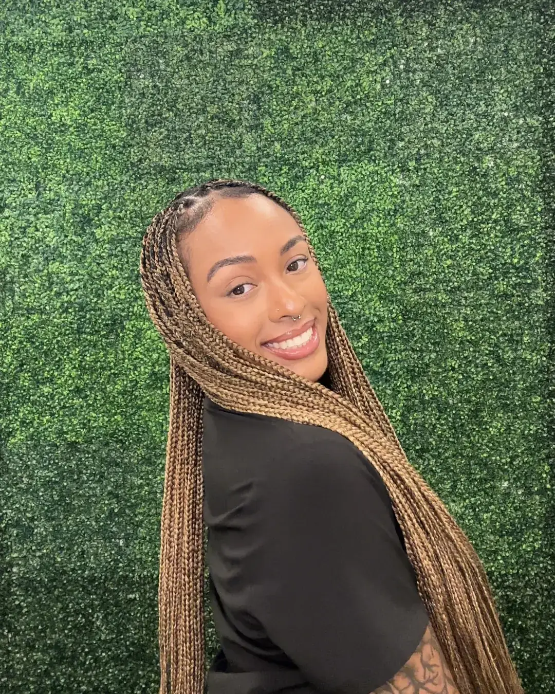 Lala, licensed esthetician and founder of Eden's Aesthetic & Co., smiling in front of a garden-green wall